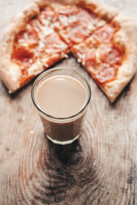 Coffee drink in a transparent glass with pizza on a wooden background. cocoa and pizza, top view.