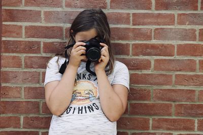 Girl taking a photo against a brick wall