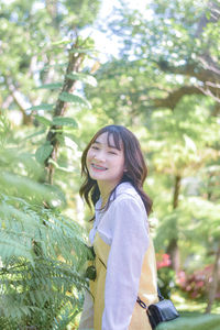 Portrait of young woman standing against trees