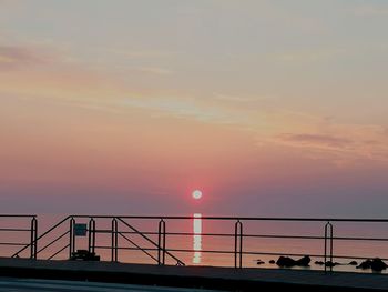 Silhouette bridge over sea against sky during sunset