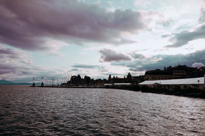 View of buildings by river against cloudy sky