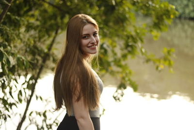 Portrait of smiling young woman standing against tree