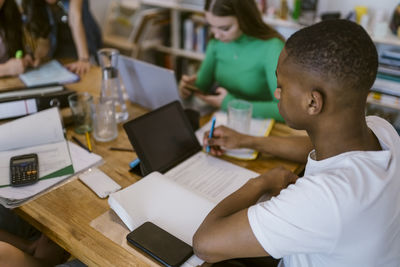 Young man reading book while doing homework at dining table