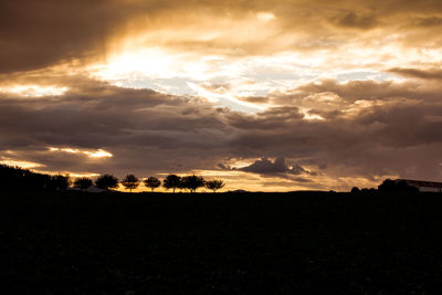 Silhouette of trees on landscape against cloudy sky