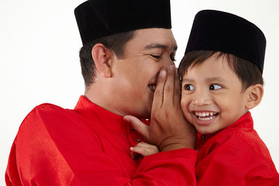 Close-up of father and son whispering against white background