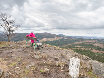 Rear view of woman walking on mountain against cloudy sky