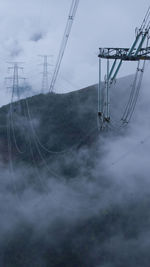 Low angle view of electricity pylon against cloudy sky