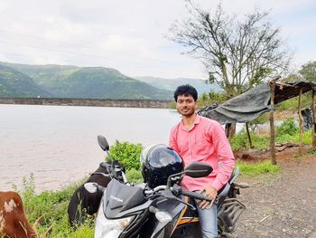 Portrait of happy young man on shore against mountains