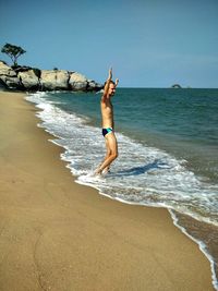 Side view of man in underwear standing with arms raised on shore at beach