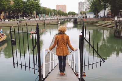 Rear view of woman standing on footpath leading towards pier at river