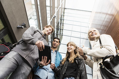 Low angle view of young friends using digital tablet in university