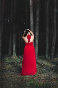 Rear view of young woman standing on tree trunk in forest