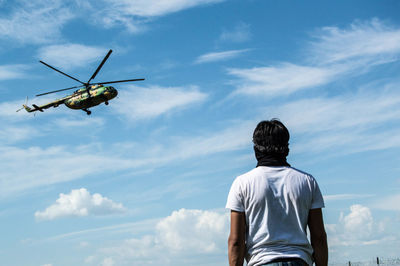 Rear view of man looking towards airplane flying in sky