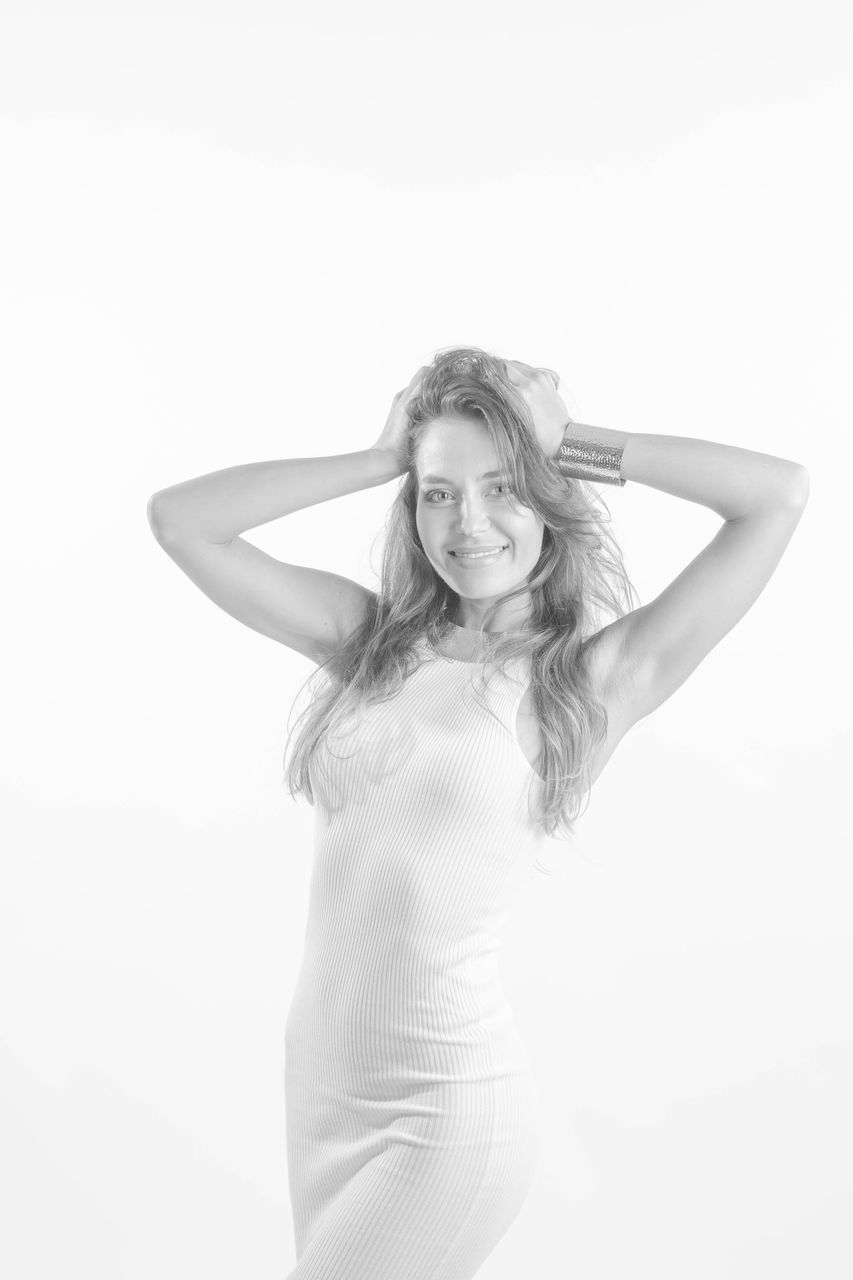 women, one person, adult, portrait, long hair, young adult, hairstyle, studio shot, fashion, white, looking at camera, clothing, black and white, elegance, blond hair, indoors, female, white background, glamour, monochrome photography, emotion, photo shoot, arm, happiness, standing, smiling, slim, copy space, human face, arms raised, limb, human hair, dress, brown hair, human limb, person, dancing, hand in hair, three quarter length, hand