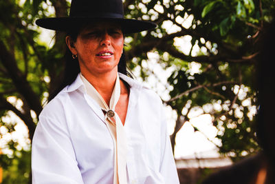 Portrait of woman wearing hat while standing against trees