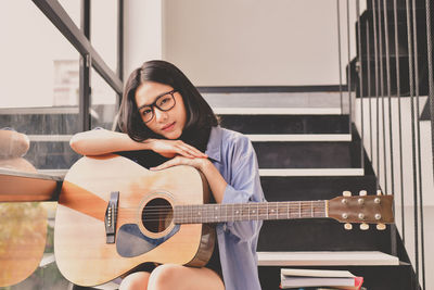 Portrait of young woman with guitar sitting on steps at home