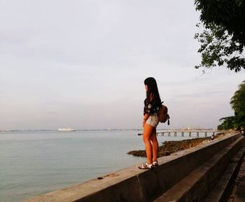 Rear view of woman standing by sea against sky