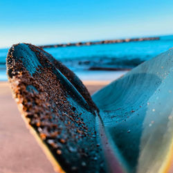 Close-up of rusty metal on beach against clear blue sky