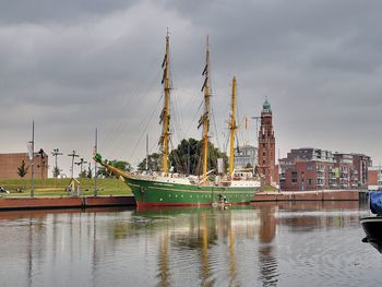 Sailboats in river by buildings against sky