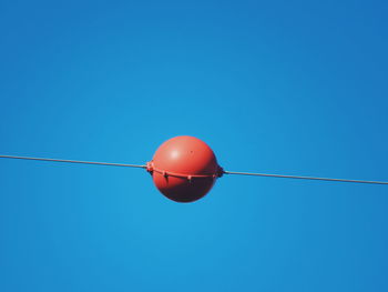 Low angle view of red ball in cable against clear blue sky during sunny day