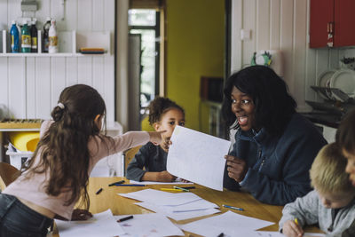 Girl pointing at teacher showing drawing during art class in day care center