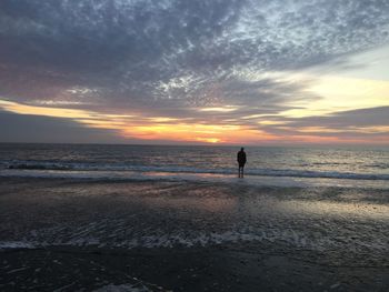 Man standing at beach against sky during sunset