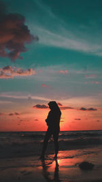 Silhouette man standing on beach against sky during sunset