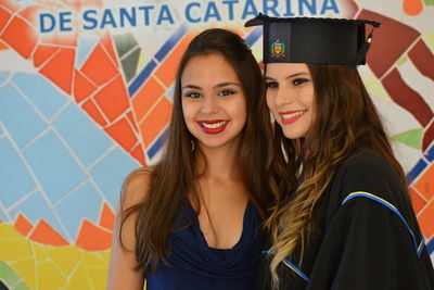 Smiling young woman with friend in graduation gown
