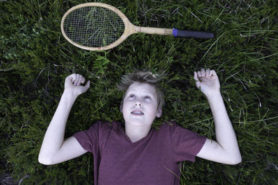 High angle view of tired teenage boy with tennis racket on grassy field