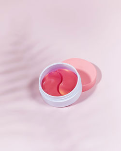 A container with pink eye patches with retinol and collagen on a pink background with a shade 