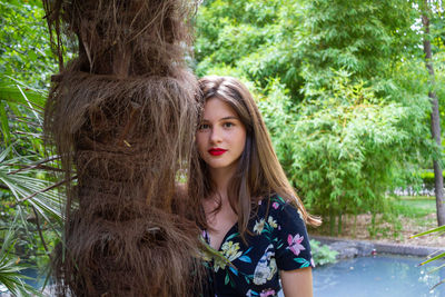 Portrait of young woman standing against tree