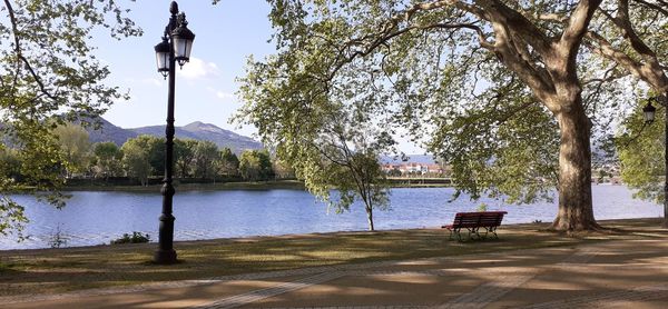 Park bench by lake against sky