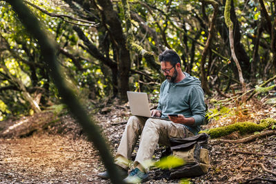 Man using mobile phone while sitting on tree trunk