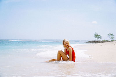 Portrait of smiling young woman sitting at beach against sky