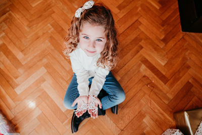 High angle view portrait of cute girl holding decoration while sitting on hardwood floor