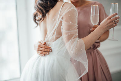 Midsection of bridesmaid and bride holding champagne flute