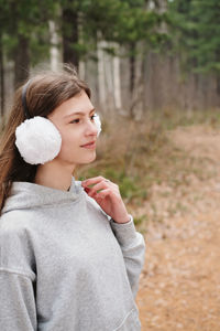 Outdoor portrait of teenager girl wearing white earmuffs. girl walking in the forest. 