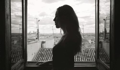 Side view of young woman standing by window at home