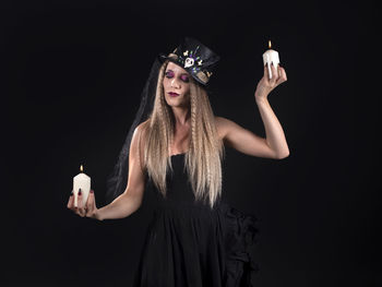 Portrait of young woman standing against black background