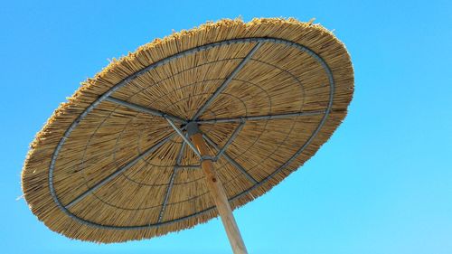 Low angle view of thatched roof parasol against clear blue sky