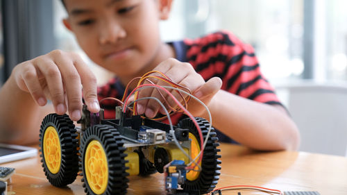 Midsection of boy repairing toy vehicle on table