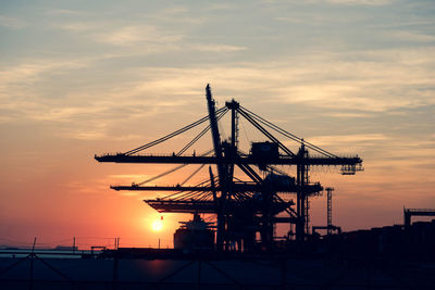 Silhouette cranes at commercial dock against sky during sunset