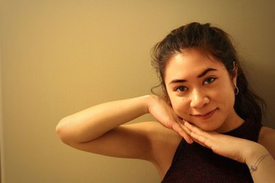 Portrait of smiling young woman with hands under chin against wall