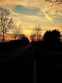 Road amidst silhouette trees against sky during sunset