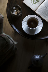 A moody mlose up with selective focus of tea cup, sugar and a book on a table.