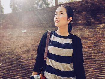 Girl looking away while standing against brick wall