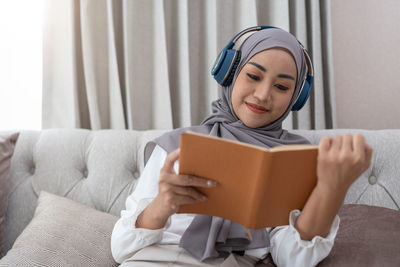 Portrait of young woman using digital tablet while sitting on bed at home