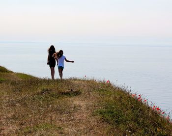 Rear view of girls walking on mountain by sea against sky