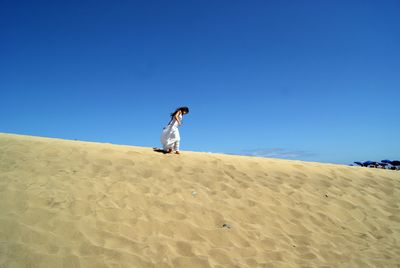 Low angle view of woman walking on sand dune at beach against clear blue sky