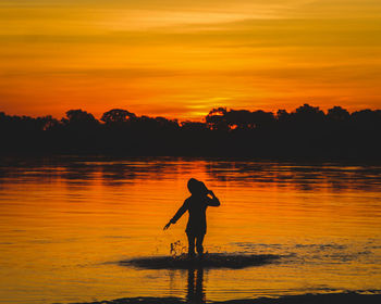 Silhouette woman standing in lake during sunset